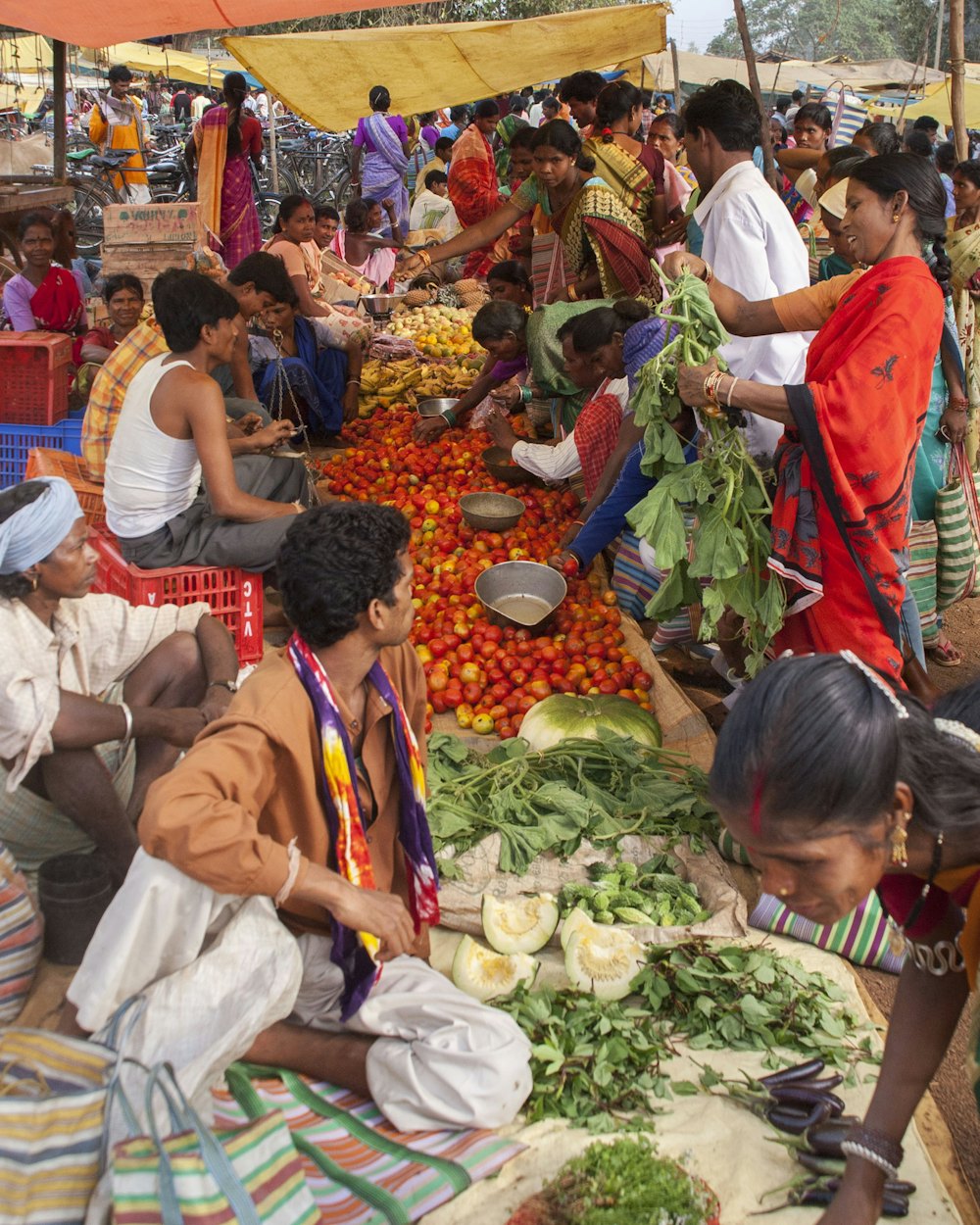 Sellers and buyers around heaps of tomatoes and greens at a local market